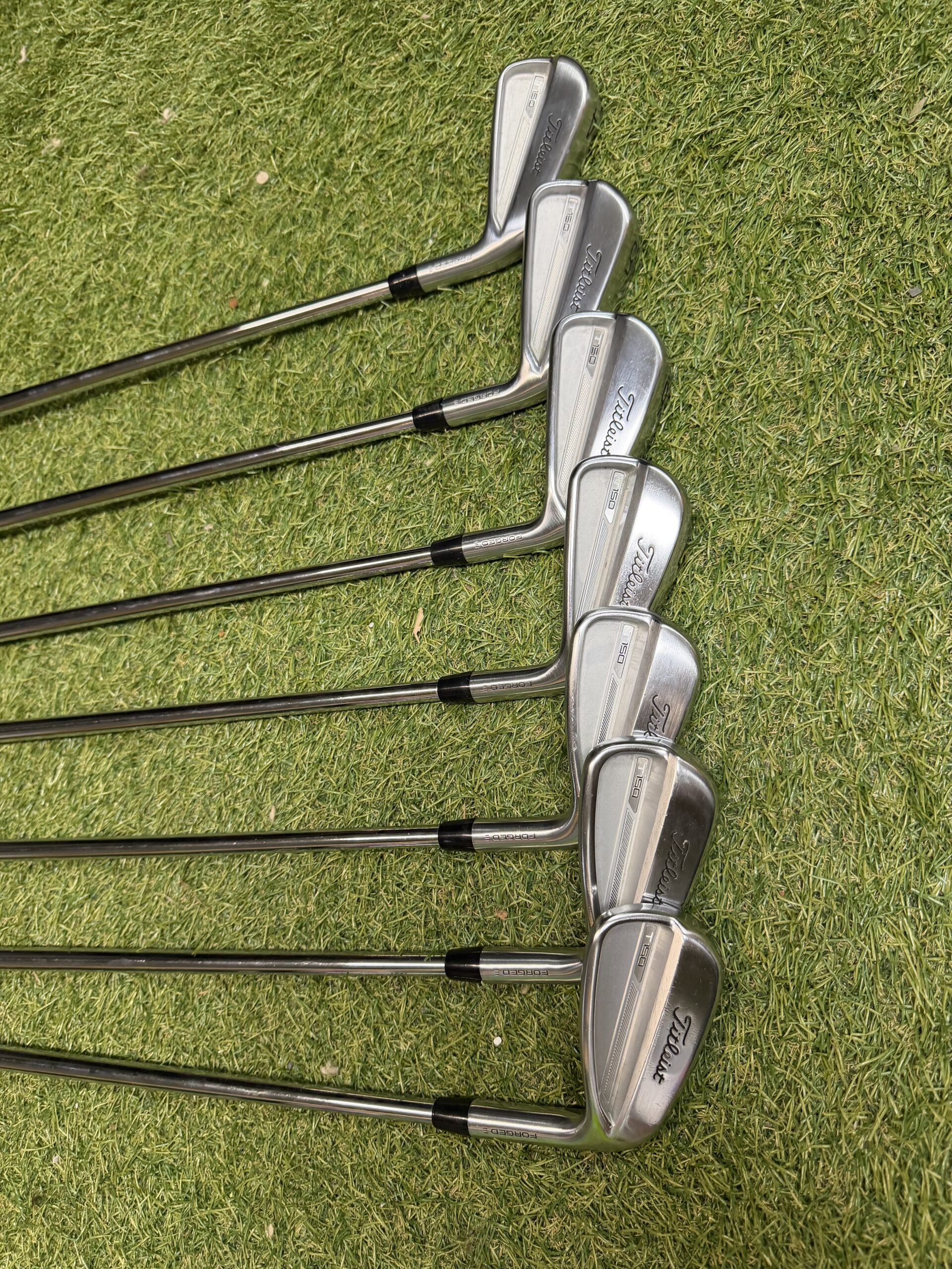 Dos de plusieurs fers Titleist alignés sur le gazon.
