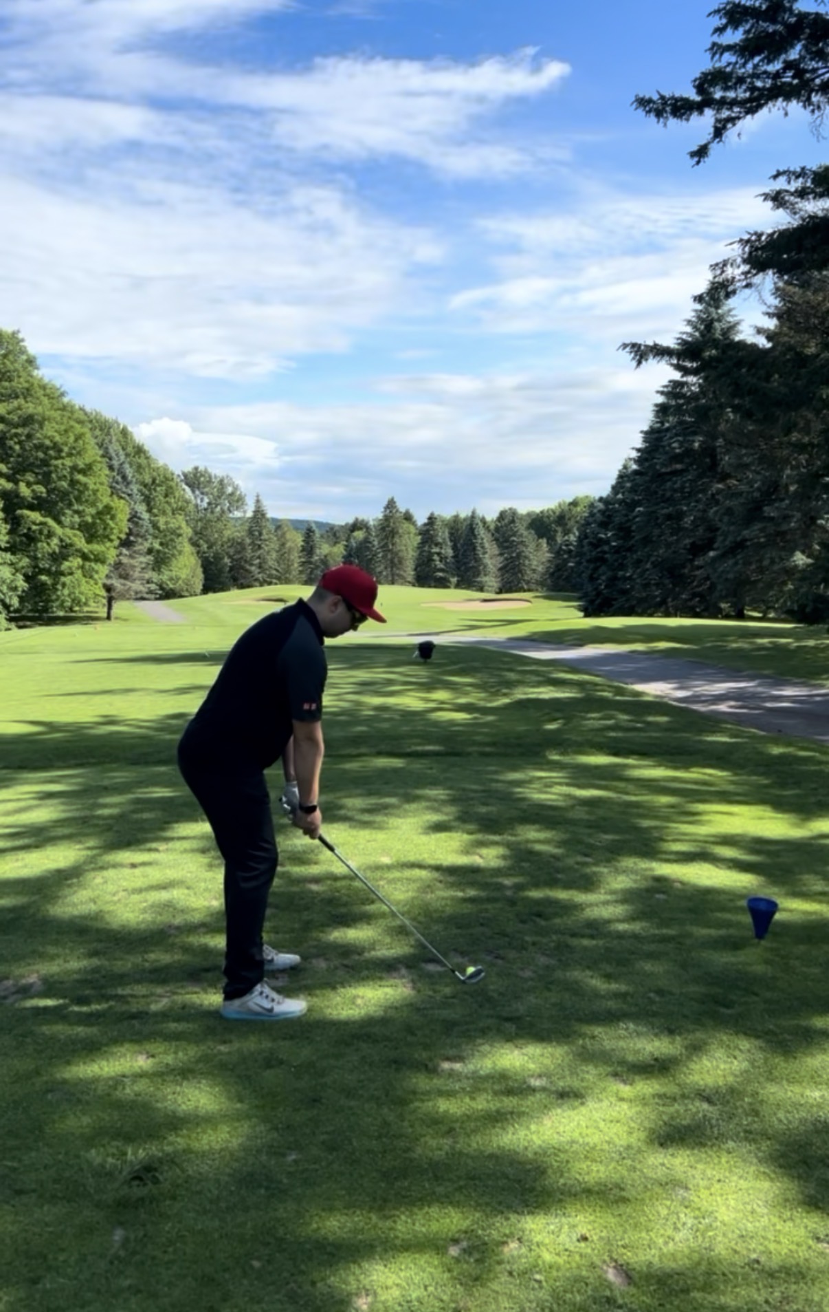 Golfeur à l’adresse sur un départ, face à une allée bordée d’arbres.